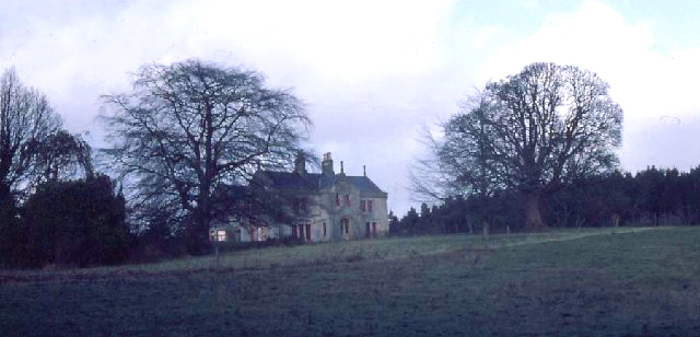 Shows a large manor on a hill obscured by trees.