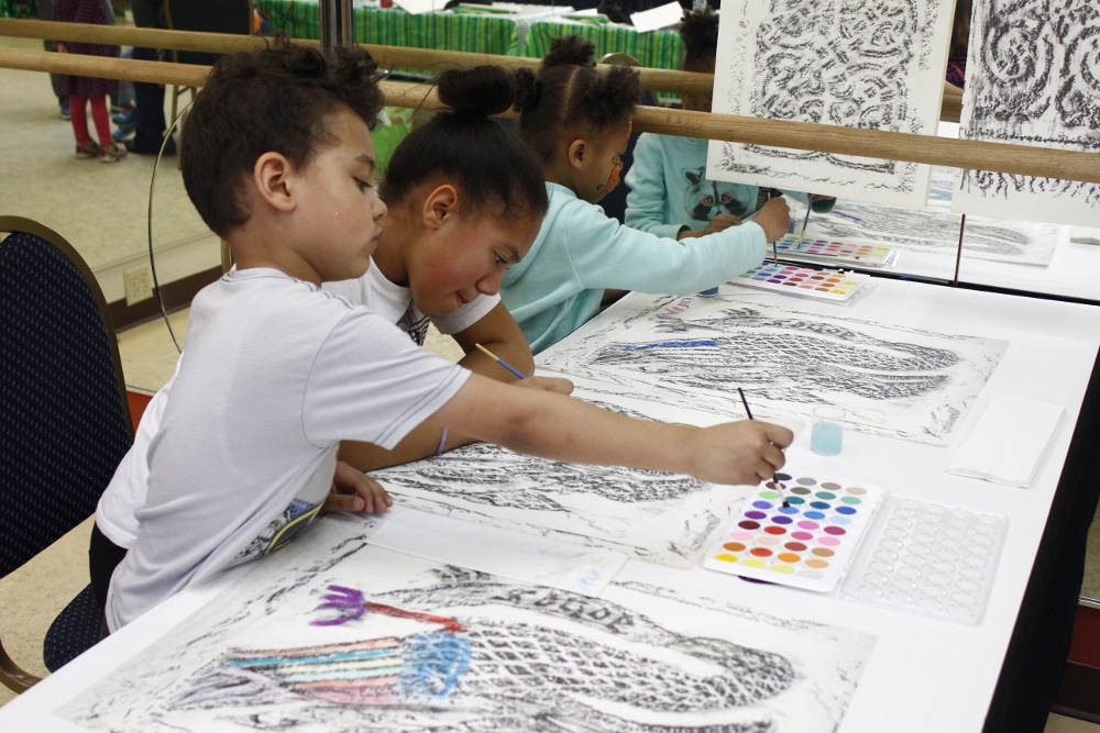 Children coloring knotwork at a table during an outreach event.