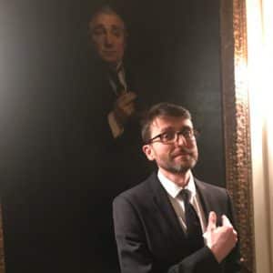 Man in suit standing in front of oil painting of man in suit