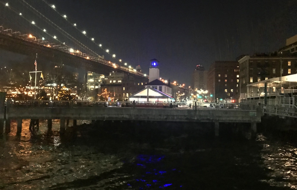 Ferry stop in NYC at night, water, Brooklyn bridge, warehouses.
